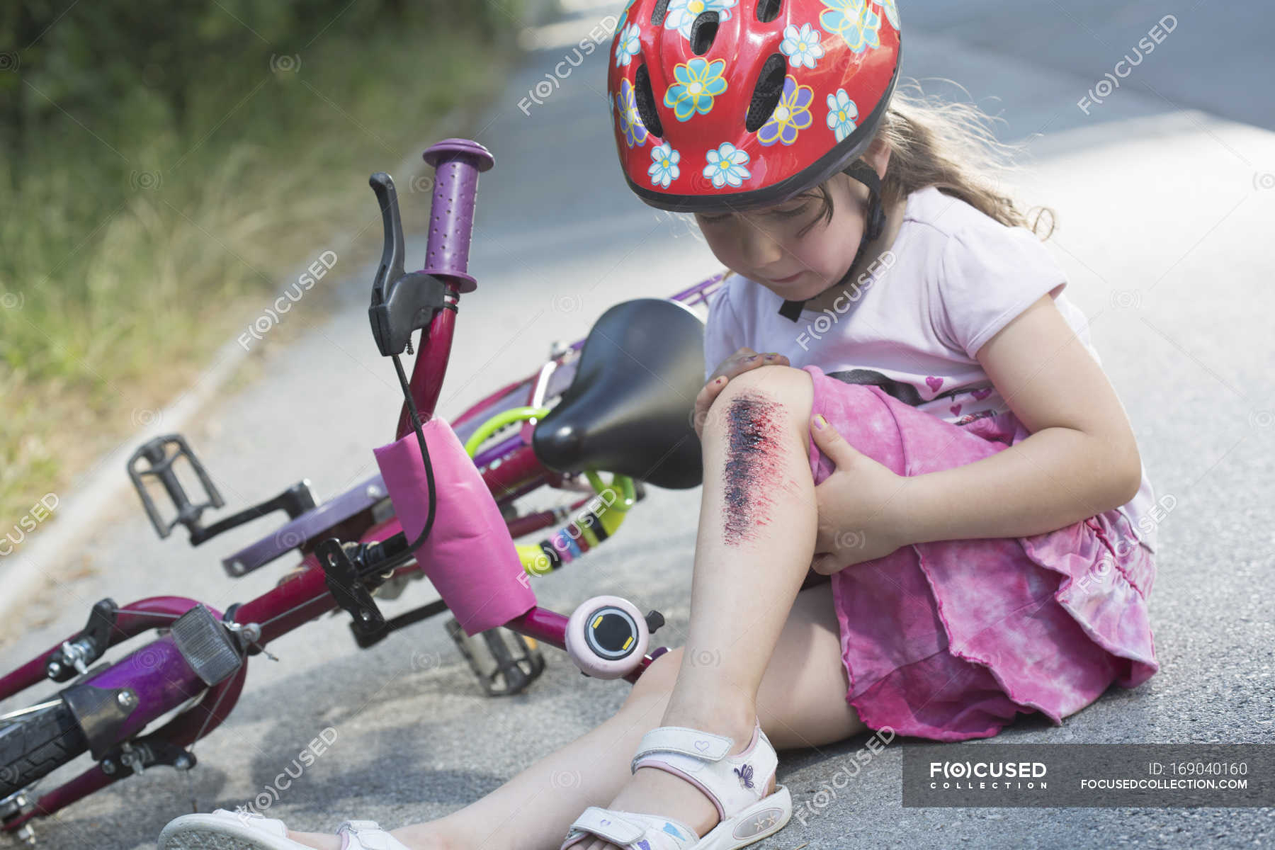 little-girl-with-injured-leg-sitting-on-road-with-bicycle-people