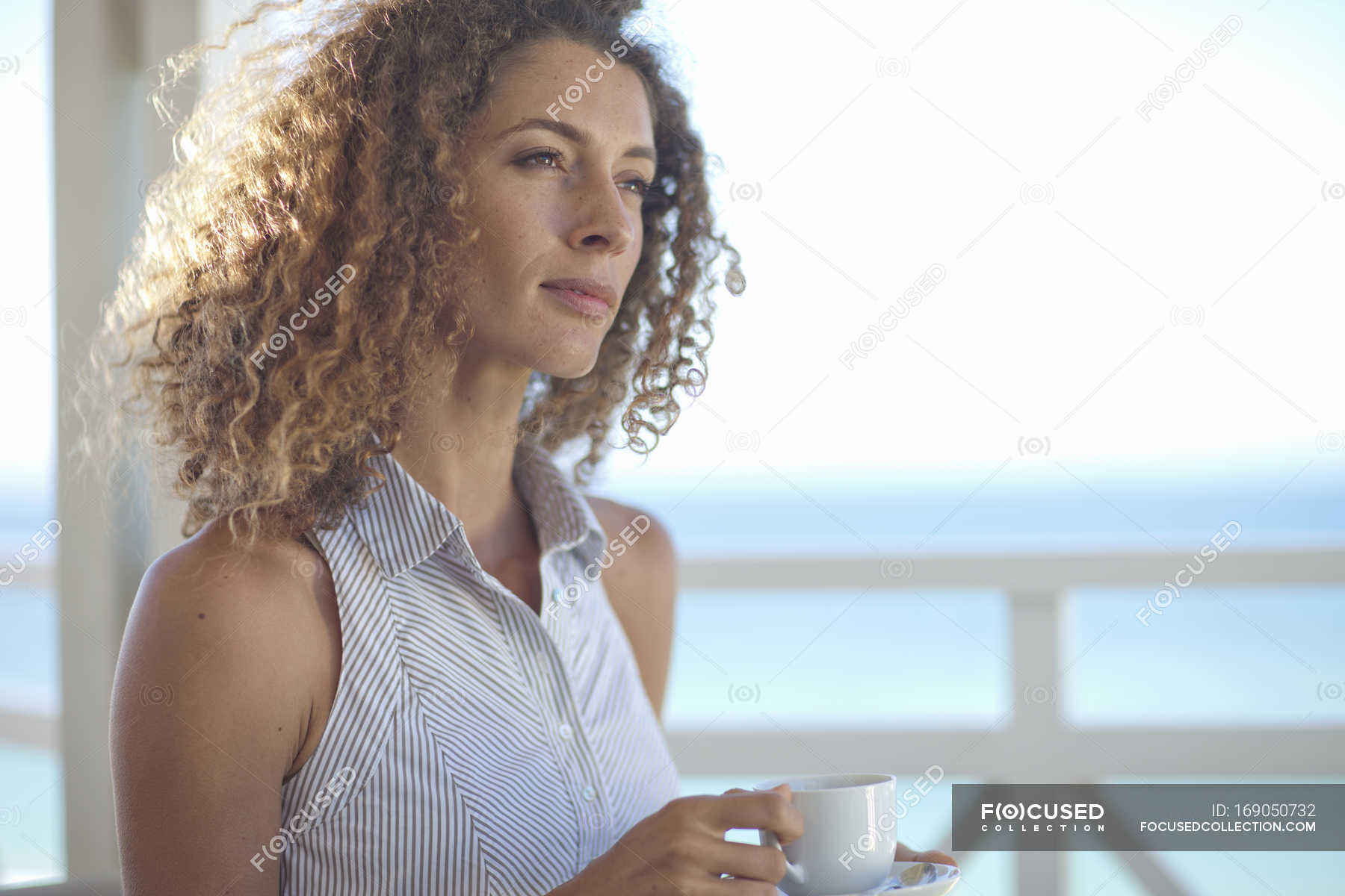 Young woman gazing out to sea from beach house balcony — buildings ...