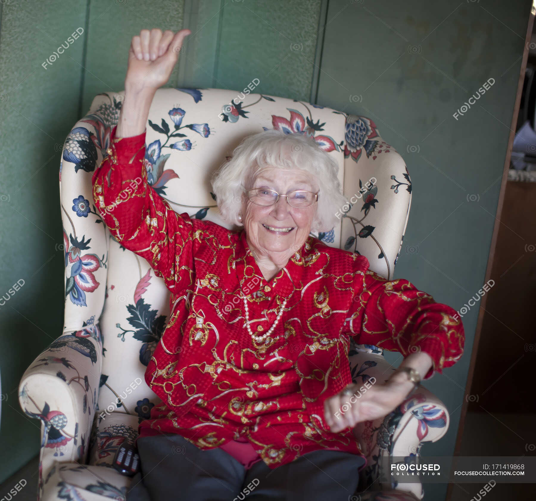 portrait-of-senior-woman-sitting-in-chair-smiling-arm-raised-female