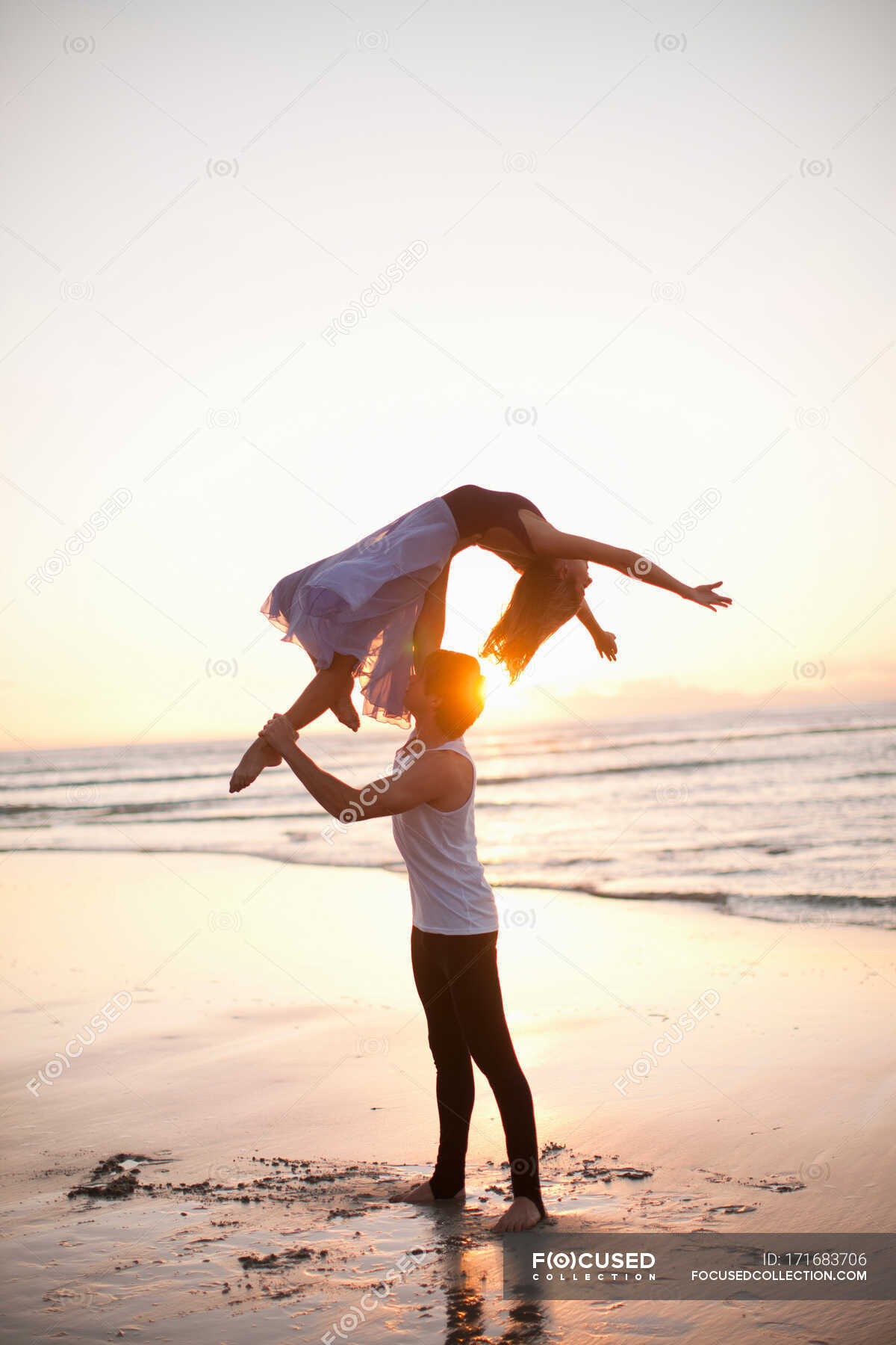 Young man lifting dancing partner on sunlit beach — love, Ballet