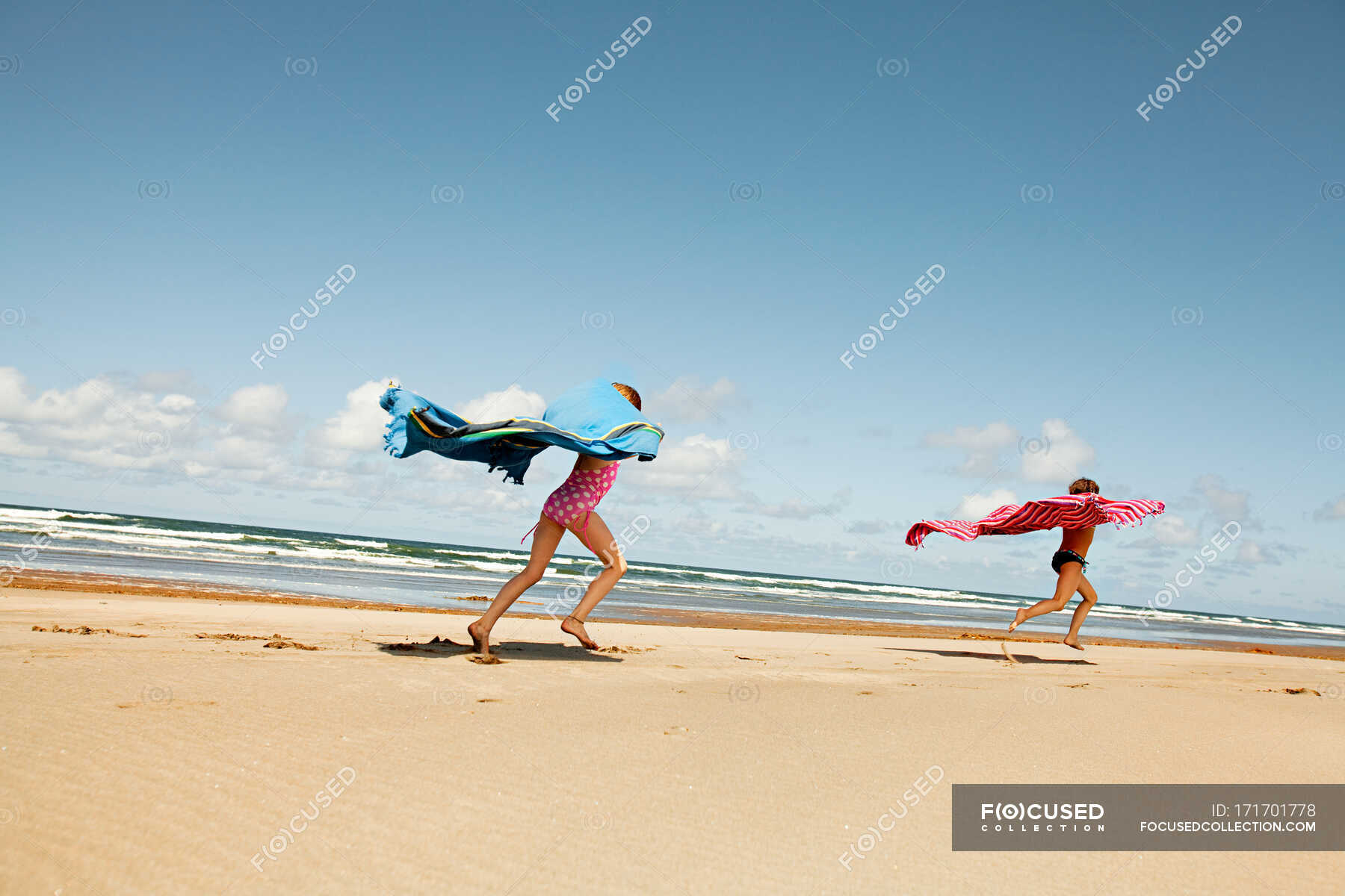 Girls running with blankets at beach — energy, wind Stock Photo