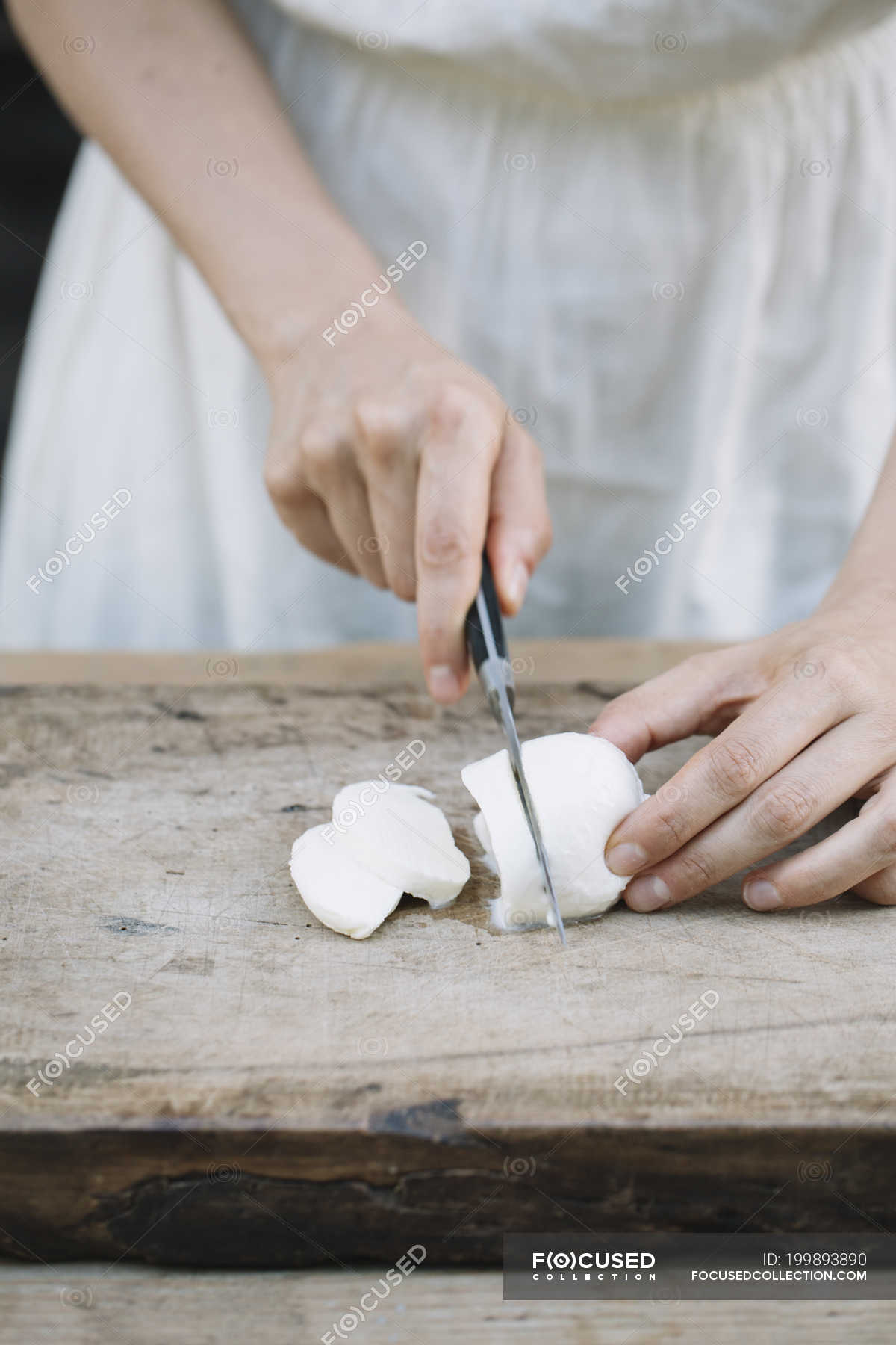 Cropped image of Woman slicing mozzarella on chopping board — faceless