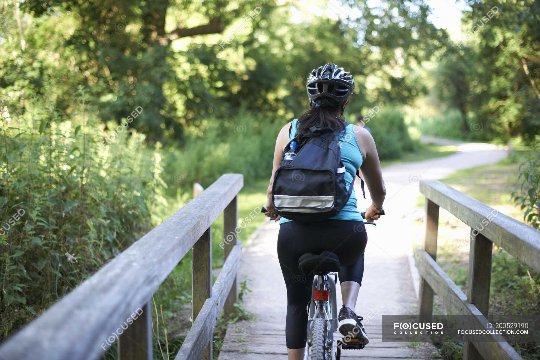 Rear view of female cyclist riding across bridge — sport, Differential ...