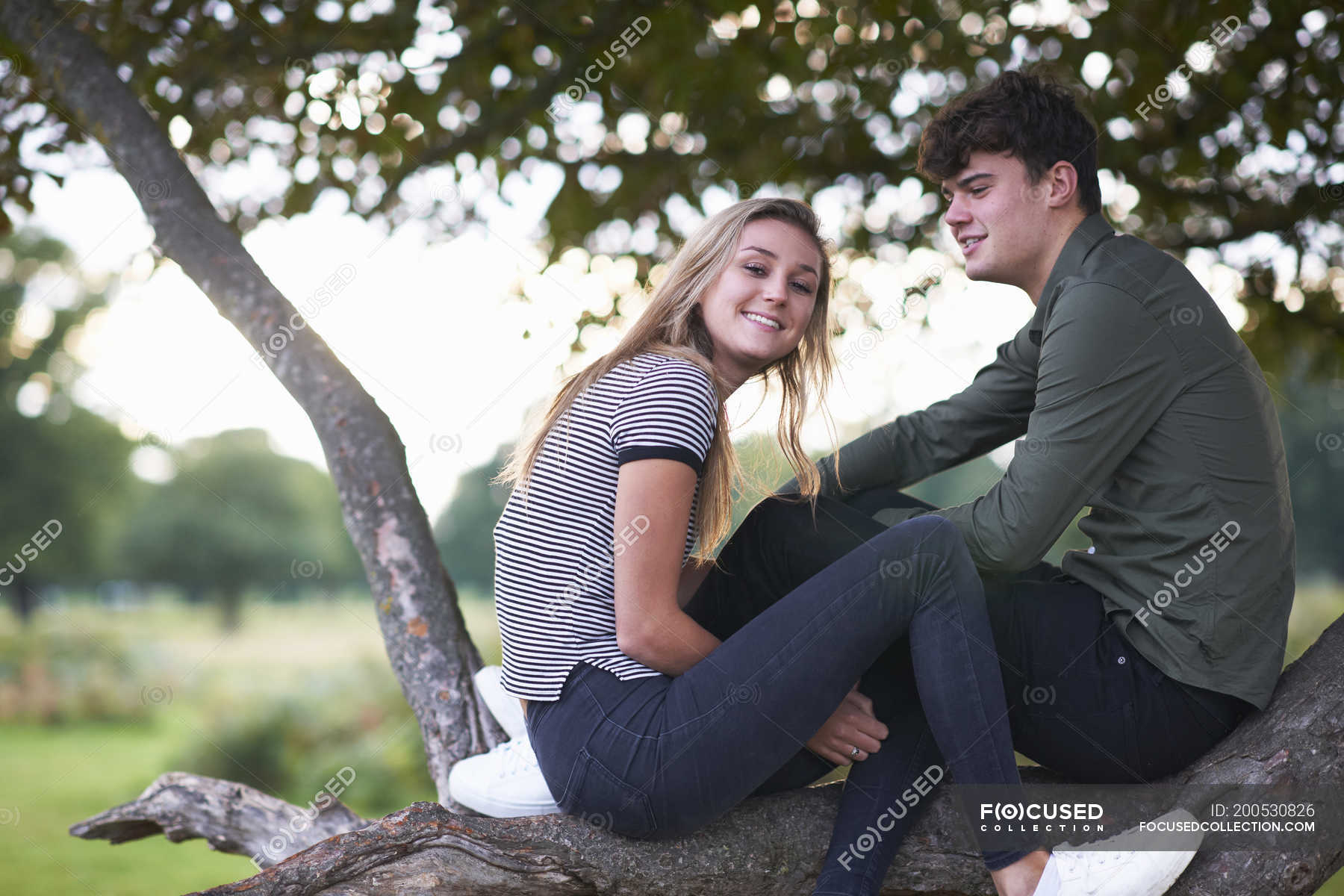 Portrait of young couple sitting on tree branch in field — people ...