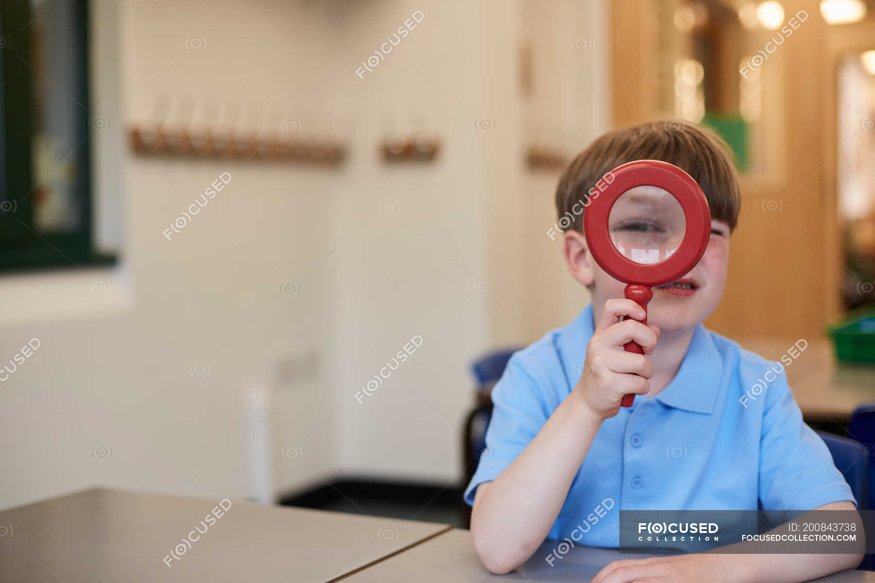 Schoolboy looking through magnifying glass in classroom at primary school, portrait — happiness