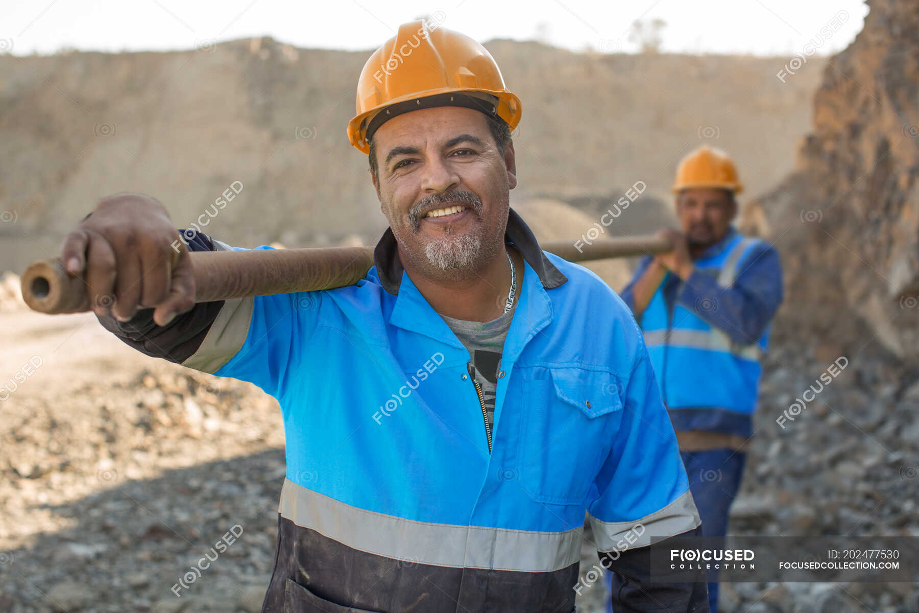 Portrait of quarry workers in quarry, carrying metal pipe — safety