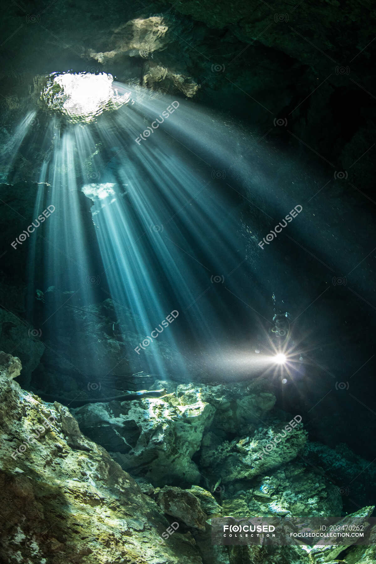 Male diver diving in underground river (cenote) with sun rays and rock ...