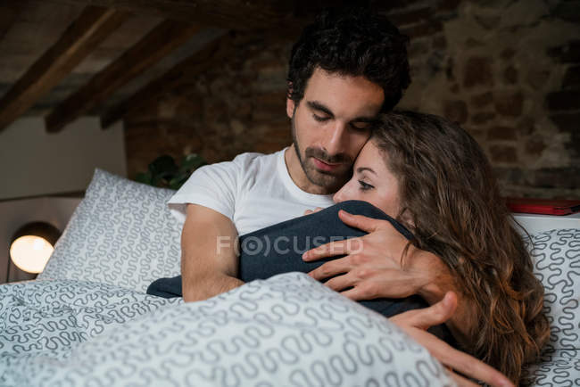 Pareja romántica acostada en la cama abrazándose - foto de stock