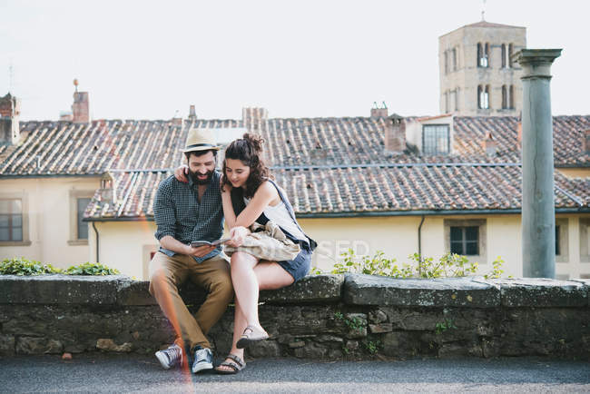 Paar sitzt an Wand und schaut sich Reiseführer an — Stockfoto