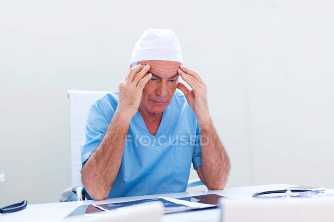Doctor en el escritorio, cabeza en las manos - foto de stock