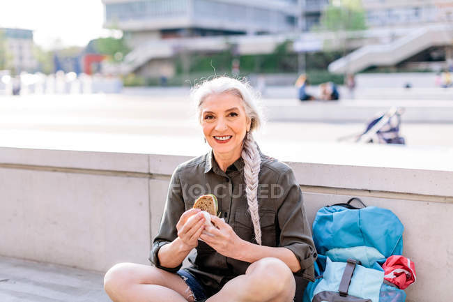 Mochileiro feminino com sanduíche na estação de ônibus — Fotografia de Stock