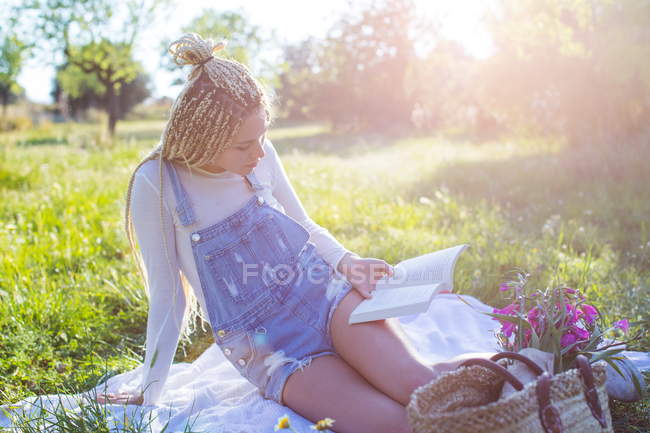 Frau liest Buch auf Picknickdecke im Feld — Stockfoto