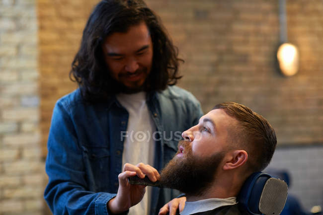Парикмахер стрижет бороду клиентам — стоковое фото