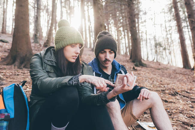 Caminhadas casal na floresta olhando para smartphone — Fotografia de Stock