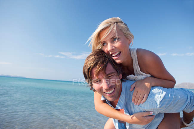 Couple playing piggyback ride by sea — Stock Photo