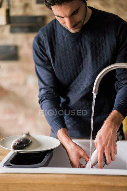 Homem lavando peixe na pia da cozinha — Fotografia de Stock