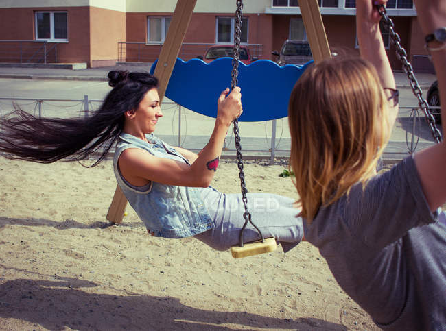 Friends swinging on playground swing — Stock Photo