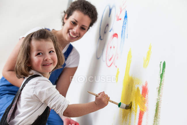 Madre e hija dibujando en pared blanca - foto de stock