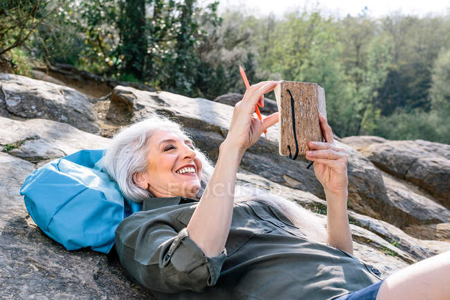 Mochileiro feminino reclinado na rocha na floresta — Fotografia de Stock