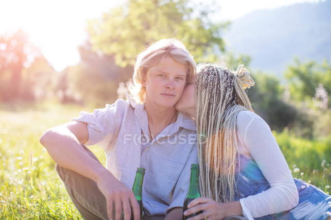 Casal sentado em campo com cerveja engarrafada — Fotografia de Stock