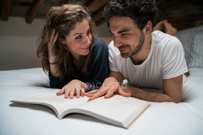 Paar liegt auf Bett und liest Buch — Stockfoto