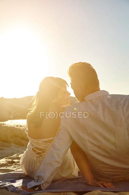 Casal sentado na praia durante o pôr do sol — Fotografia de Stock