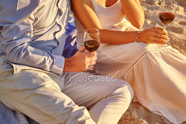 Pareja bebiendo vino tinto en la playa - foto de stock