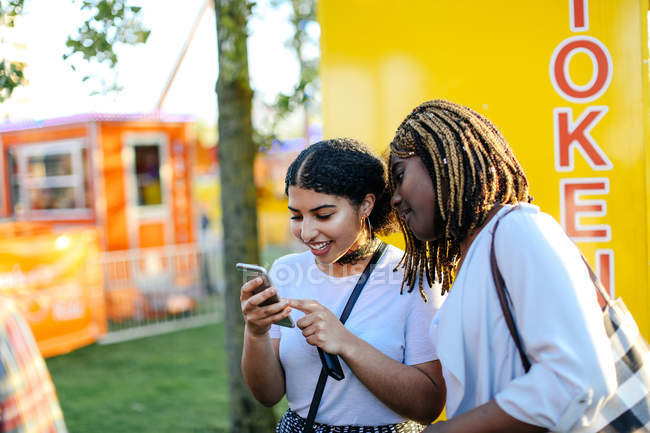 Duas meninas na feira de diversão, olhando para o smartphone — Fotografia de Stock