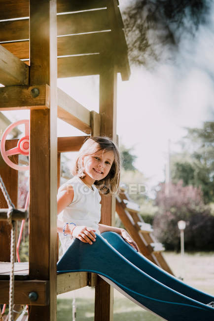Girl sitting at top of park slide and smiling — Stock Photo