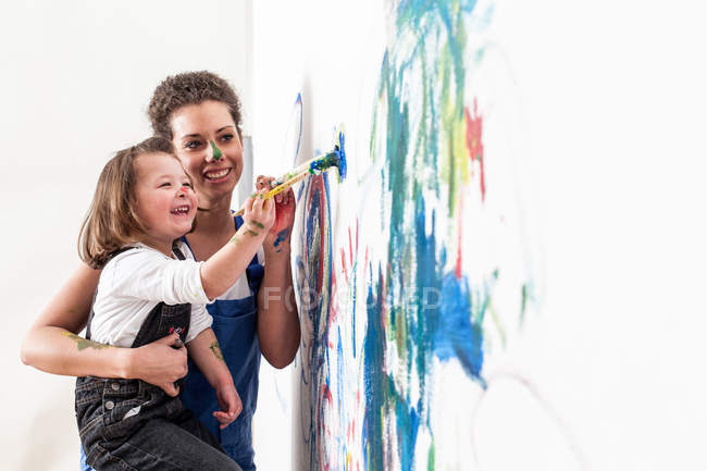 Мать и дочь рисуют на белой стене — стоковое фото