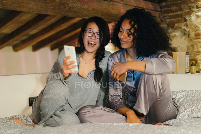 Друзі сидять на ліжку і дивляться на смартфон — стокове фото