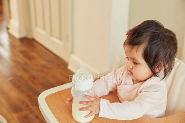 Bébé fille tenant bouteille de lait — Photo de stock