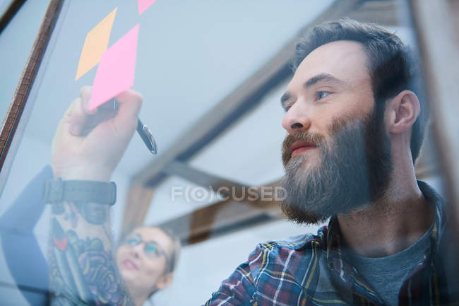 Male designer writing on adhesive note — Stock Photo