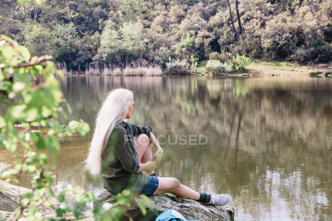 Mochileiro olhando para fora da margem do rio na floresta — Fotografia de Stock