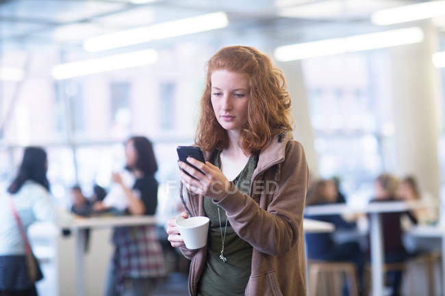 Studentin benutzt Handy in Bibliothek — Stockfoto