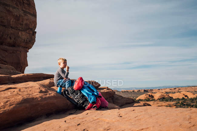Мальчик сидит на скале в пустыне, ест закуски, Моаб, Юта, США — стоковое фото