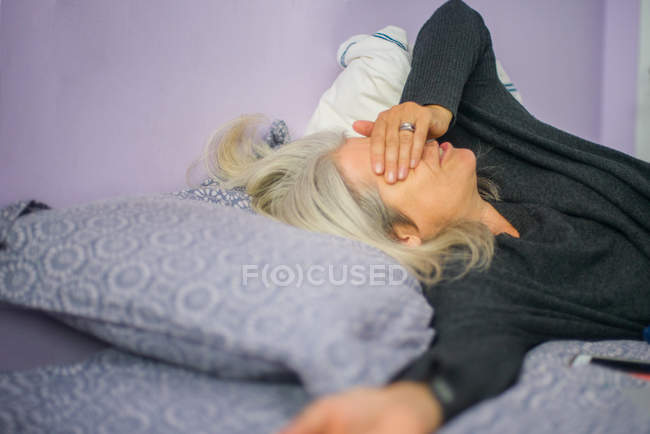 Mujer acostada en la cama y cerrando los ojos con la mano - foto de stock
