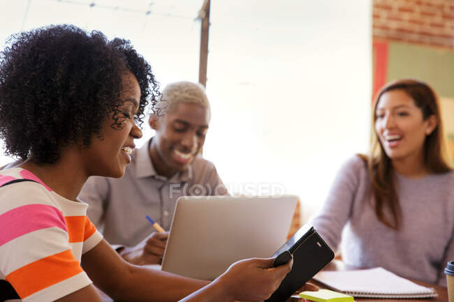 Tres colegas sentados en la mesa, usando laptop y smartphone - foto de stock