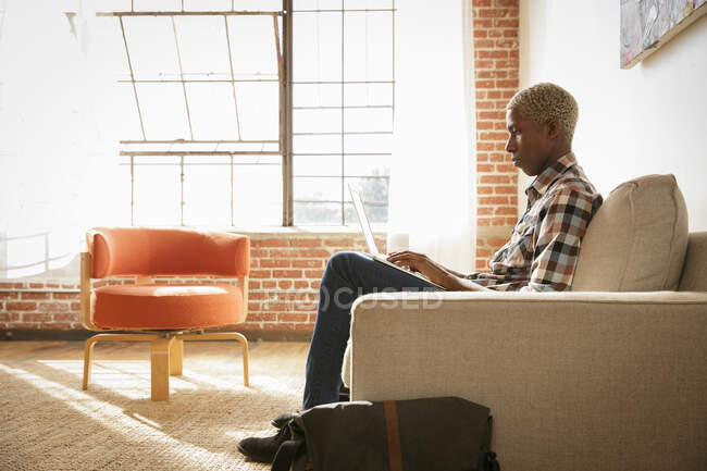 Молодий чоловік сидить на дивані, використовуючи ноутбук — стокове фото