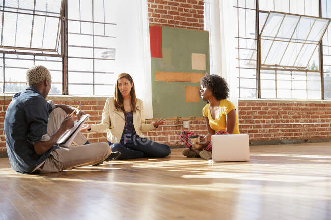 Três colegas sentados no chão em novo espaço de escritório, tendo discussão — Fotografia de Stock