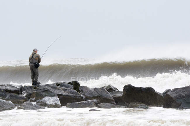 Человек, ловящий рыбу со скал в бурных океанских волнах, Лонг-Бич, Нью-Йорк, США — стоковое фото