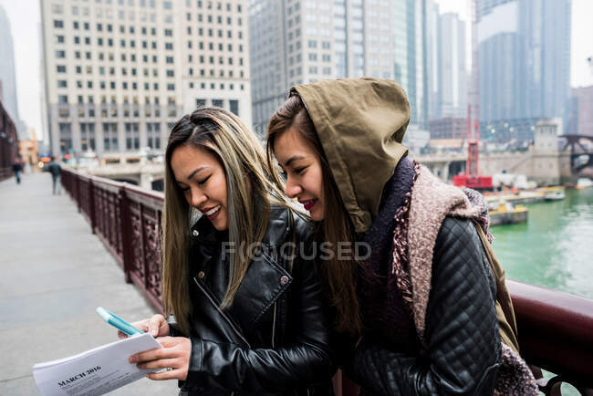 Two friends, outdoors,  looking at smartphone, smiling — Stock Photo