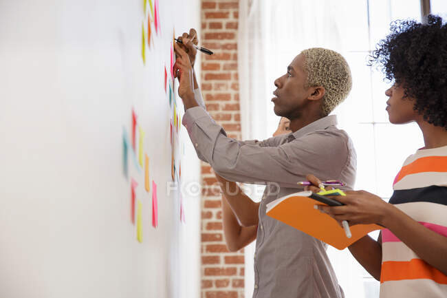 Two colleagues writing on sticky notes on whiteboard — Stock Photo