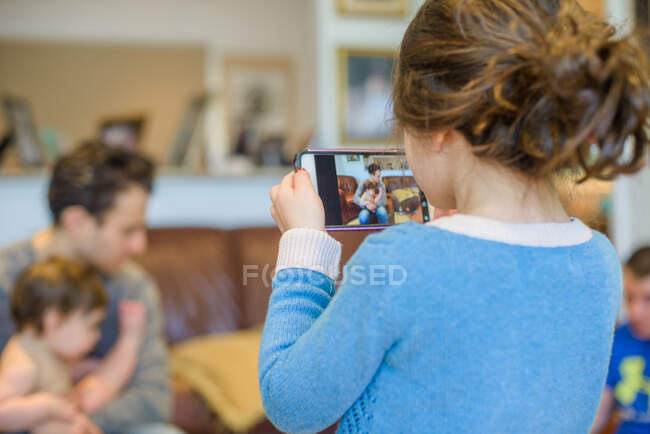 Chica fotografiando familia en sala de estar - foto de stock
