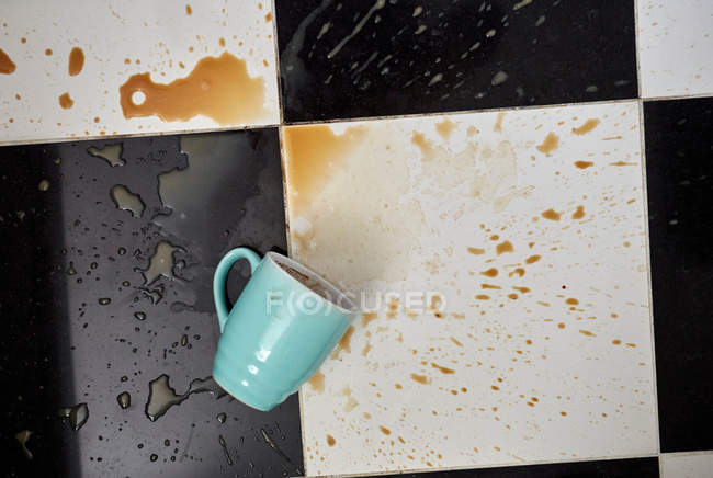 Copa en el suelo rodeado de café derramado - foto de stock