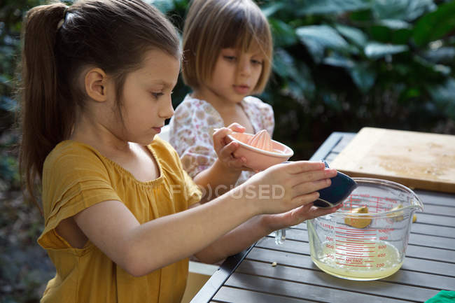Two young sisters pouring lemon juice for lemonade at garden table — Stock Photo