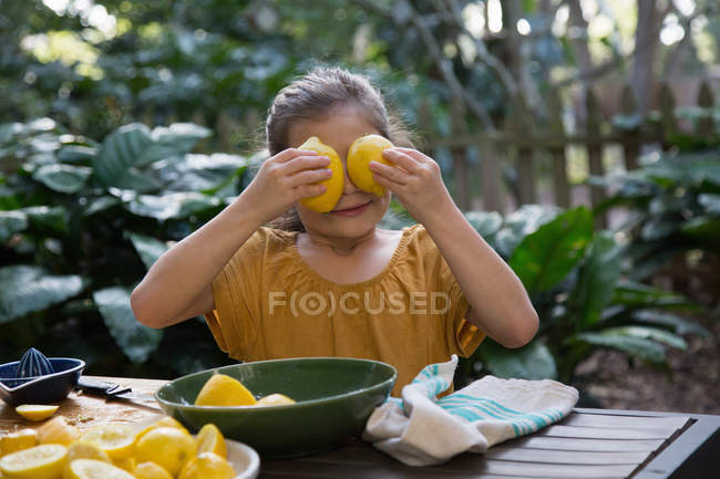 Дівчина тримає лимони на очах за садовим столом — стокове фото