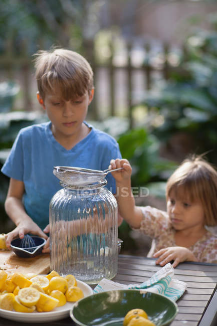 Boy and two young sister preparing lemon juice for lemonade at garden table — Stock Photo