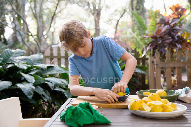 Chico exprimiendo limón para limonada en la mesa del jardín - foto de stock