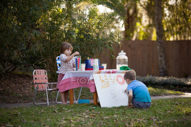 Menino e irmã preparando limonada stand sinal no jardim — Fotografia de Stock